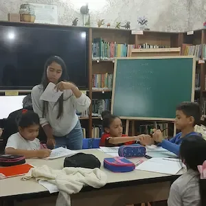 Educadora ajuda crianças em atividades escolares na Biblioteca de Copacabana, Rio de Janeiro.