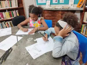 Instrutor orienta crianças durante oficina de desenho na biblioteca comunitária de Copacabana, Rio de Janeiro.